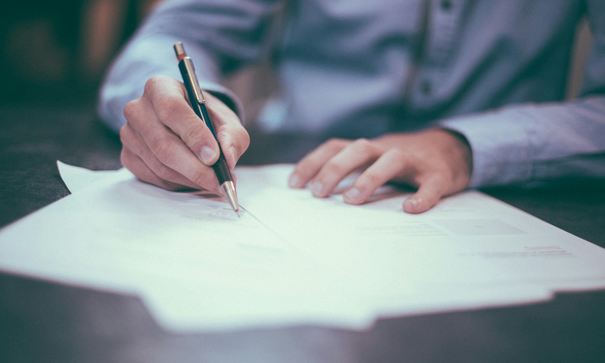 man wearing blue shirt writing with fancy pen.